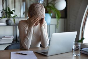 A woman holds her face while sitting in front of a laptop. Anxiety treatment in Greenwood Village, CO can offer support from the comfort of home. Search online anxiety treatment in Greenwood Village, CO or anxiety therapist near me to learn more.