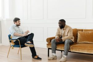 A Male therapist in a therapy session with an African American male while sitting adjacent to each other. Learn more from a depression therapist in Greenwood Village, CO. Depression treatment in Greenwood village, CO is here for you.